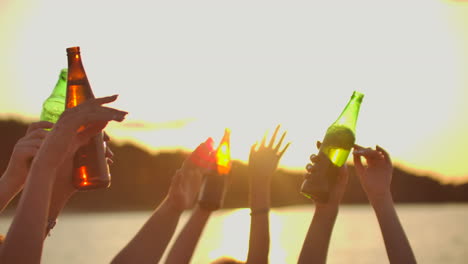 Company-of-young-people-are-dancing-with-hands-up-with-beer.-This-is-perfect-party-at-sunset-on-the-lake-coast.